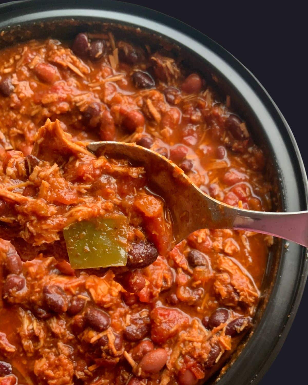A around black bowl filled with chili with a spoon picking some of it up.